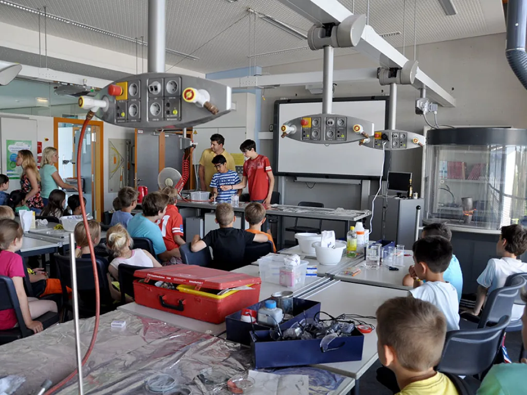 Blick in den Chemieraum, in dem Kinder an mehreren Tischen arbeiten.